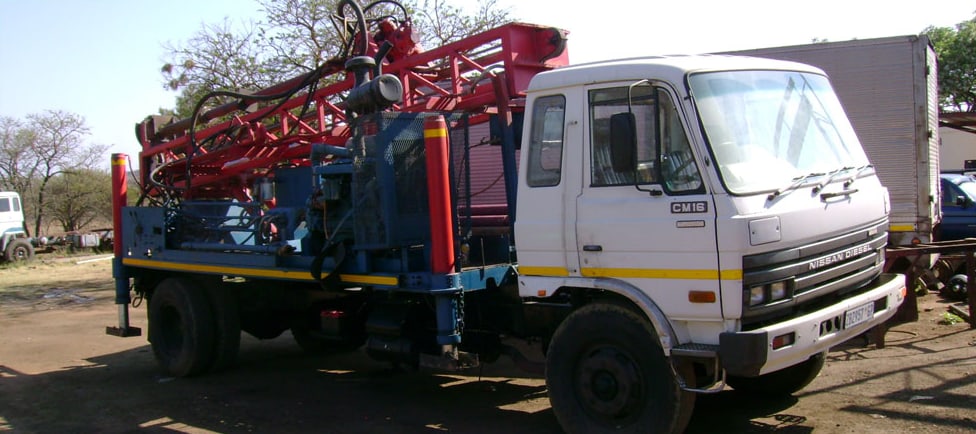 Red drilling rig mounted on a Nissan truck at the yard